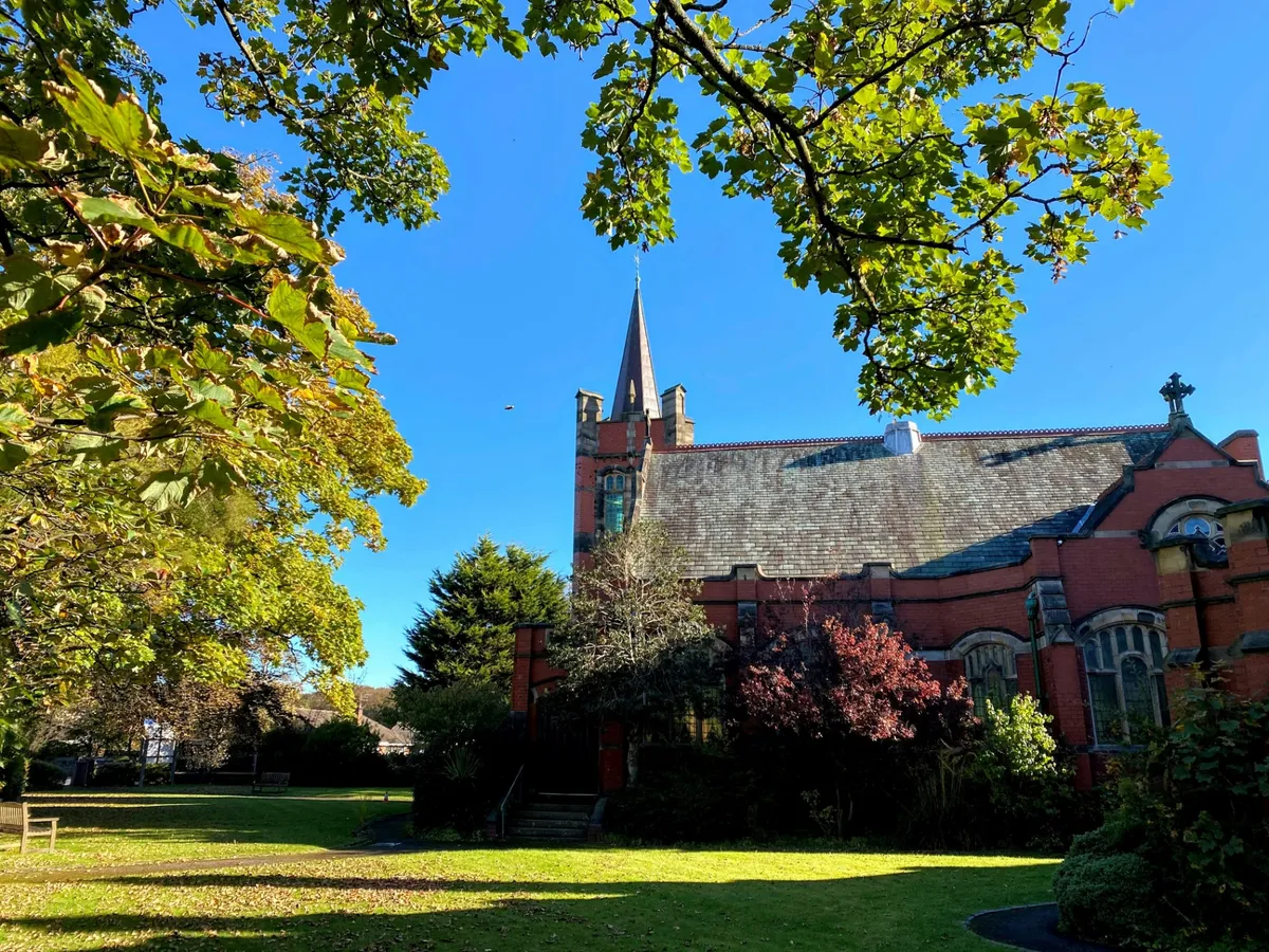 Red-brick church framed by trees and garden grounds